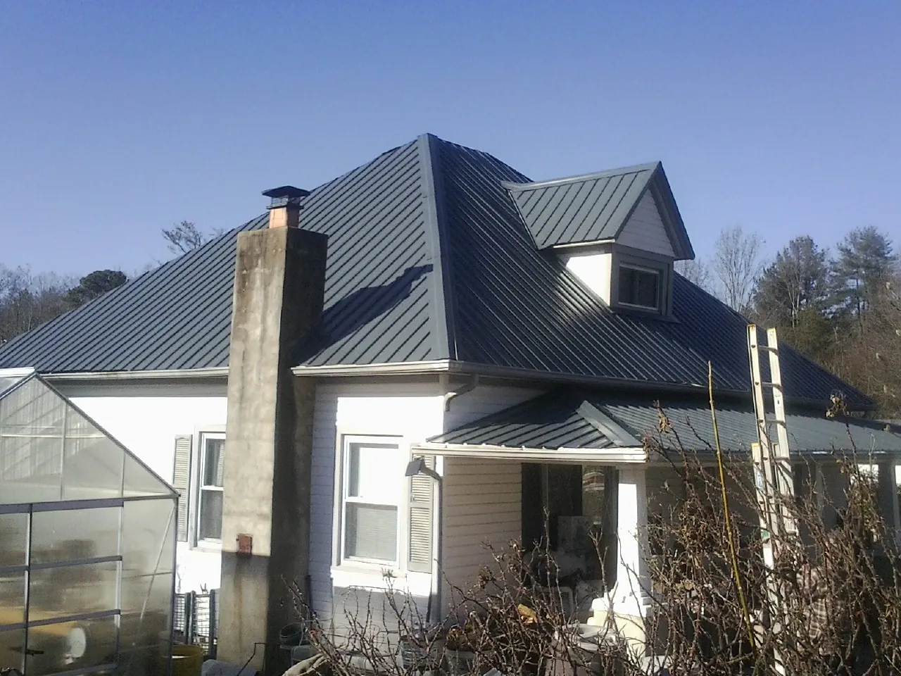 Dark blue standing seam metal roof on a white farmhouse with dormer — Slate & Tile Roof Repair by Roofing Brothers in Van Buren