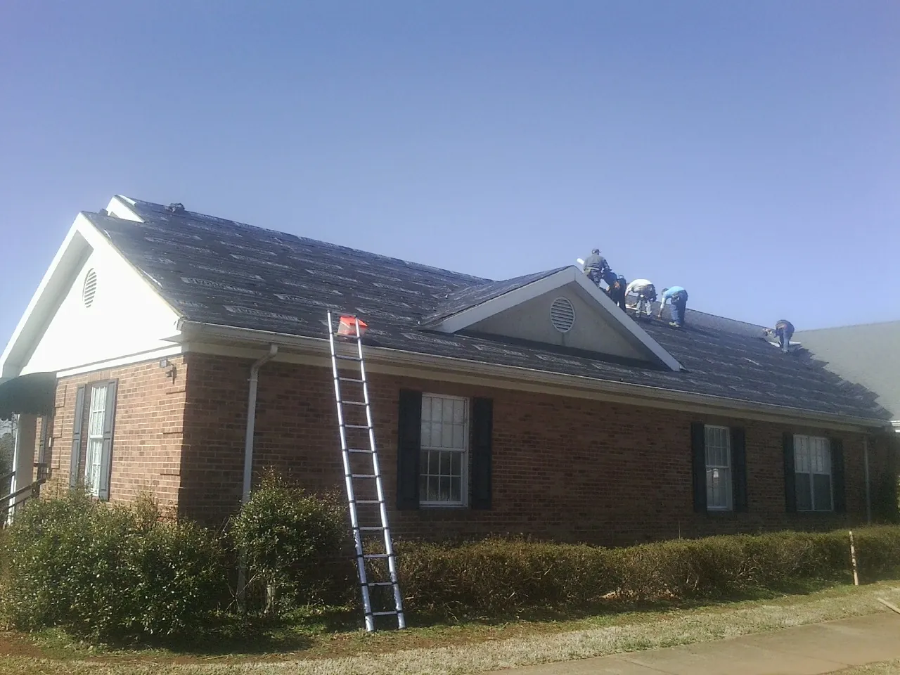 Crew tearing shingles off a brick ranch roof with a ladder set — Metal Roof Repair work by our crew in Van Buren