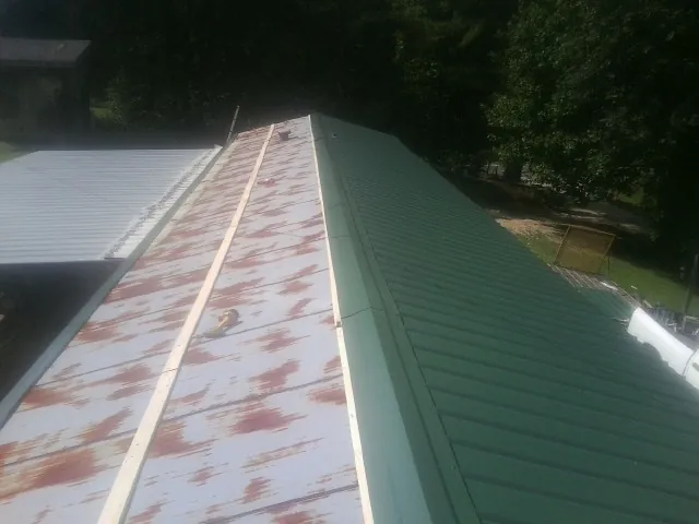 Old rusted panels beside newly installed green metal roofing — Wind Damage Roof Repair by Roofing Brothers in Van Buren