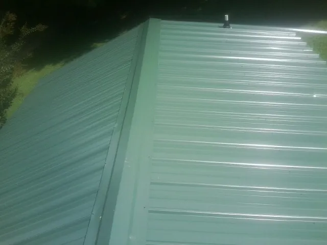 New green metal panels meeting at the ridge of a roof — Flat Roof Repair work by our crew in Van Buren