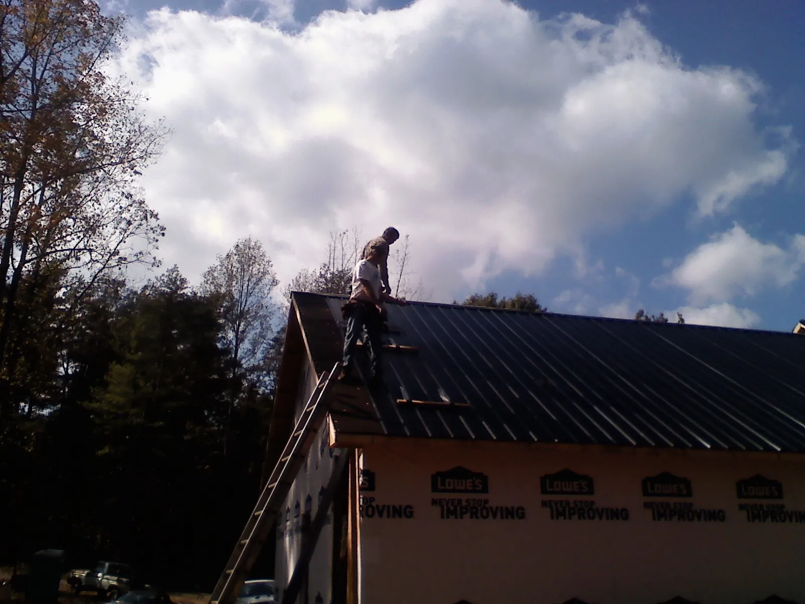 Roofer fastening dark metal panels high against a cloudy sky, from a Roof Inspection job in Van Buren