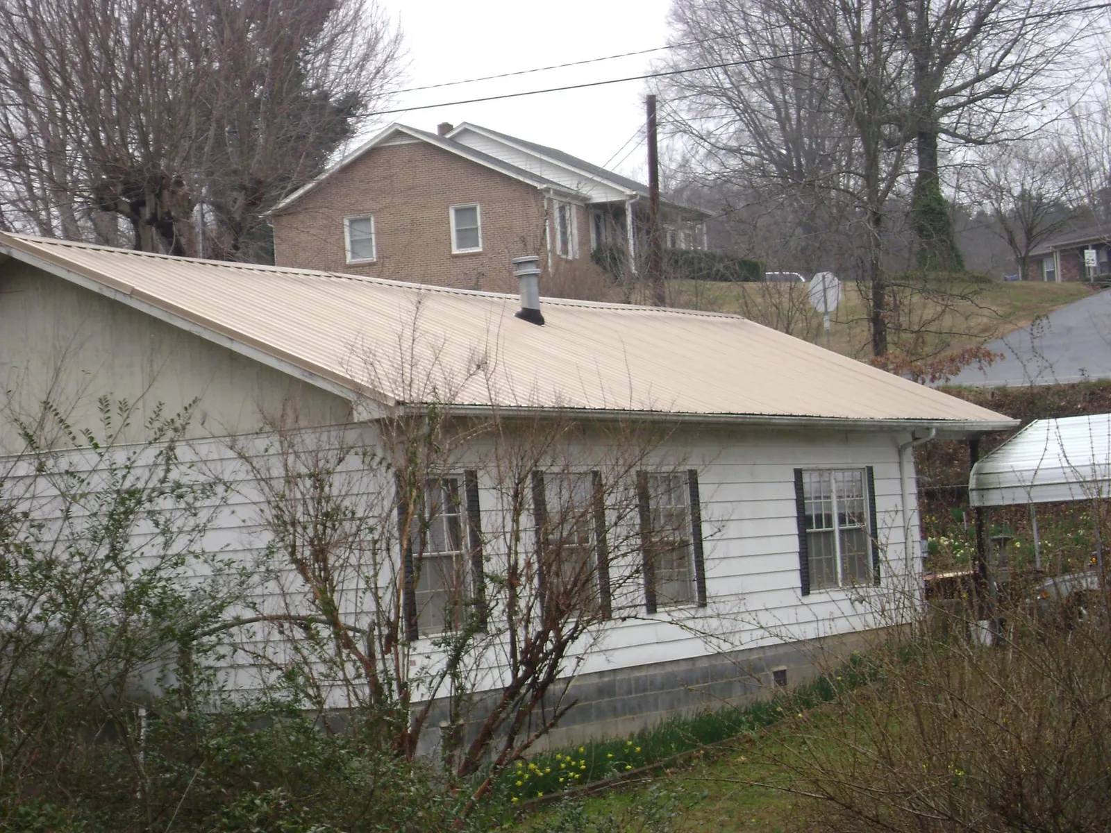 Tan metal roof on a white sided house set into a hillside — Commercial Roofing by Roofing Brothers in Van Buren